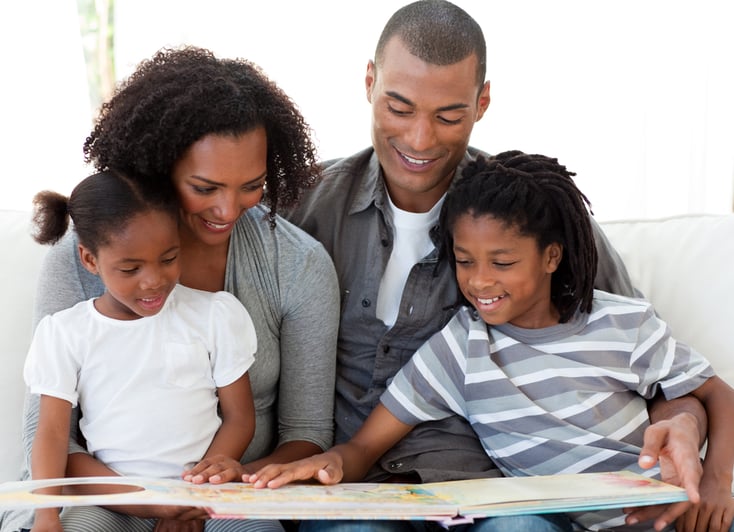 Smiling Afro-American family reading a book in the living-room