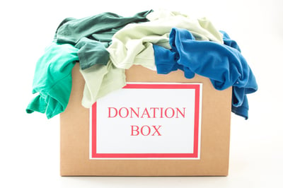 Cardboard donation box with clothes on white background