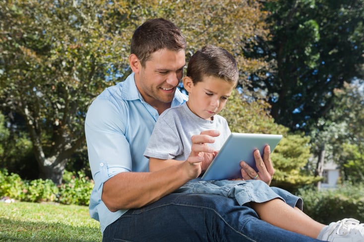 Dad and son using a tablet pc in a park on sunny day