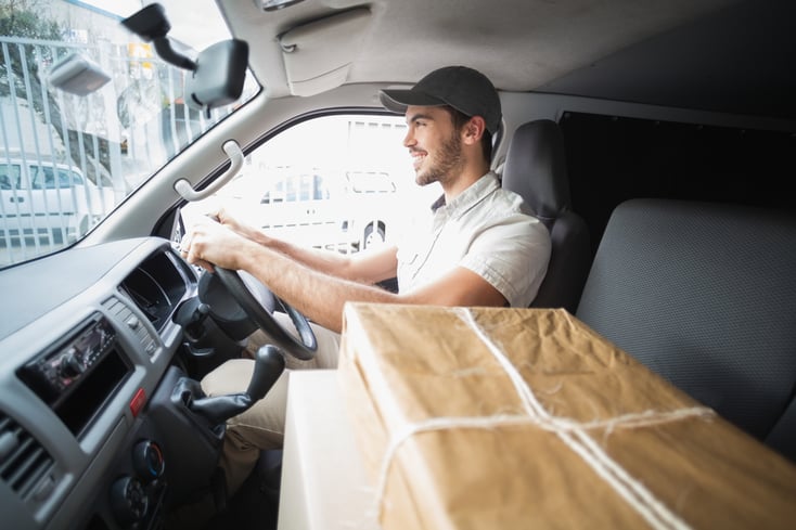 Delivery driver driving van with parcels on seat outside the warehouse