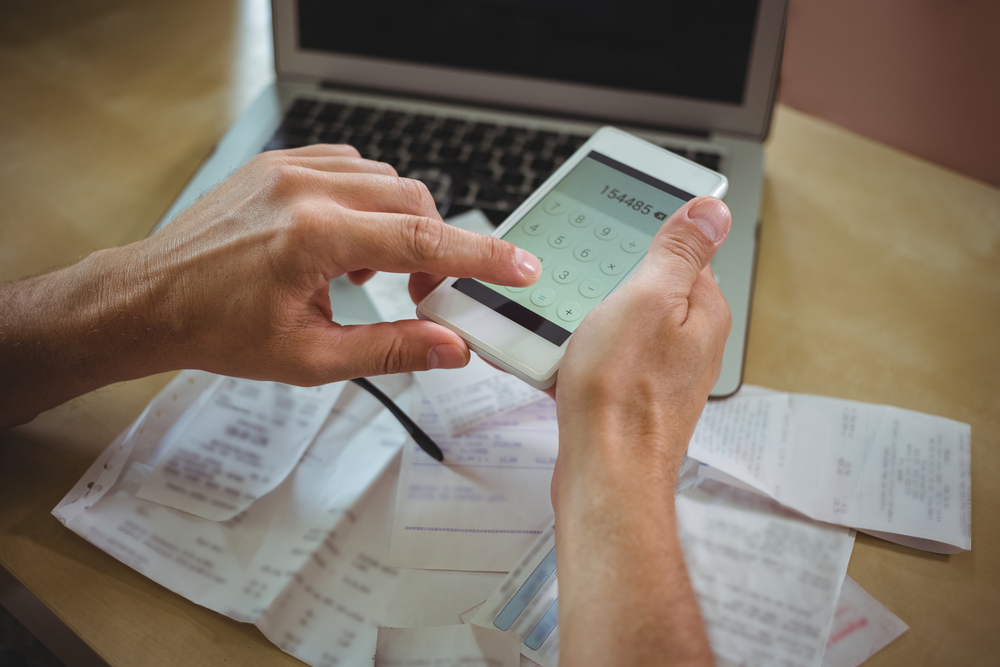 Mid section of man calculating bills on mobile phone-1