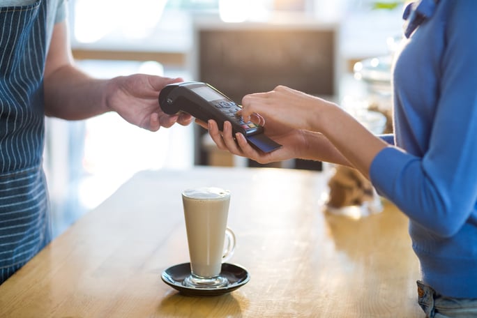 Mid-section of customer making payment through payment terminal at counter in cafx92xA9