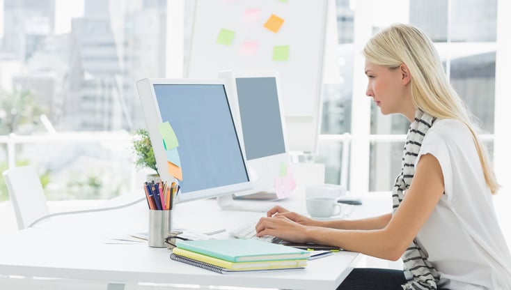 Side view of a casual young woman using computer in a bright office