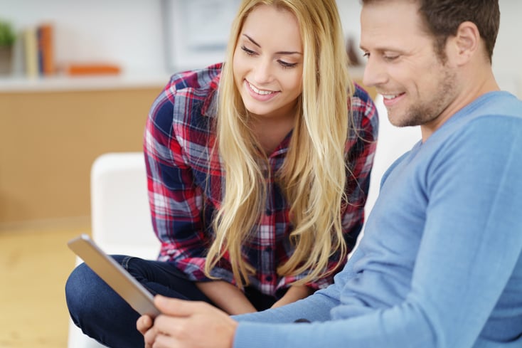 Young couple surfing the internet on a tablet computer smiling as they read information online while relaxing together on a sofa