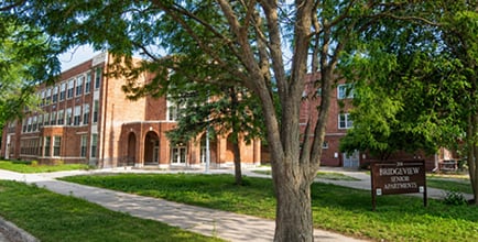 Historic brick university building with ivy-covered walls surrounded by mature trees and green lawn